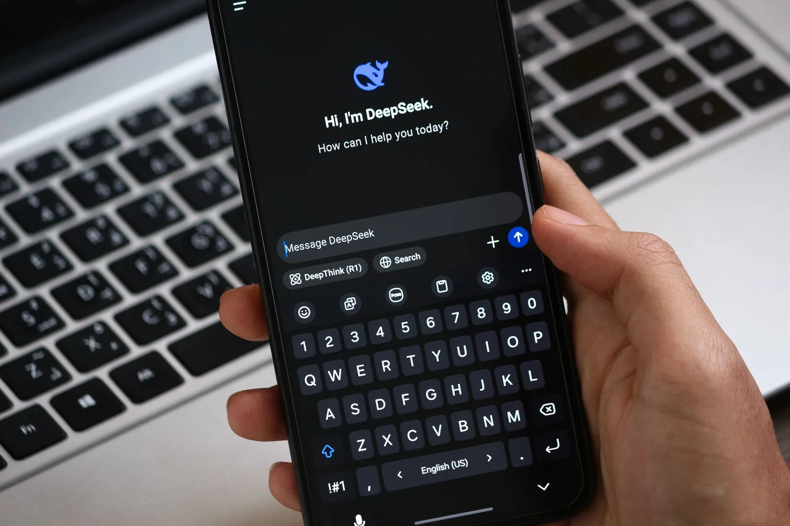 Hand met een smartphone waarop een AI-chat openstaat, boven een toetsenbord