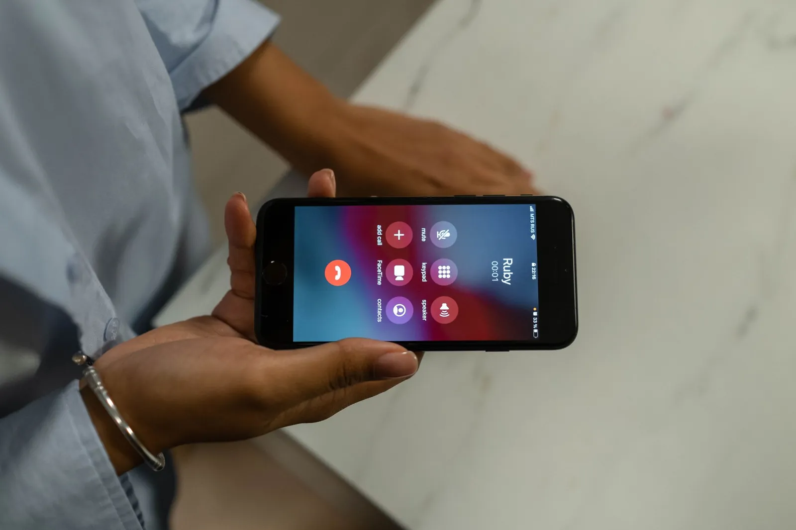 Handen met een smartphone tijdens een telefoongesprek, boven een marmeren tafel