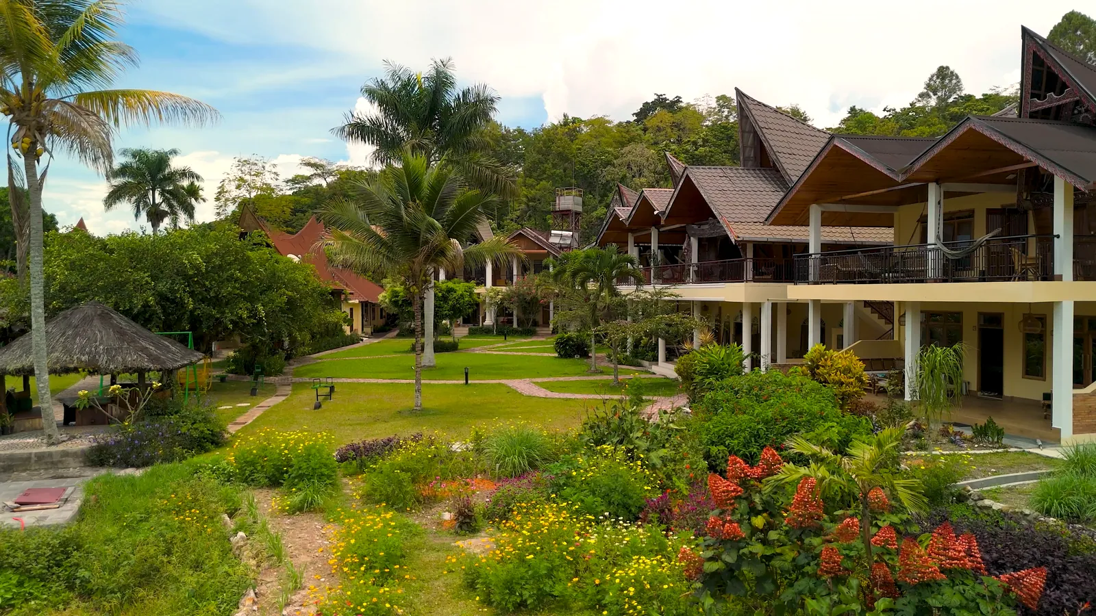 Resort met lodges, palmbomen en een tuin vol bloemen, gefilmd met een drone