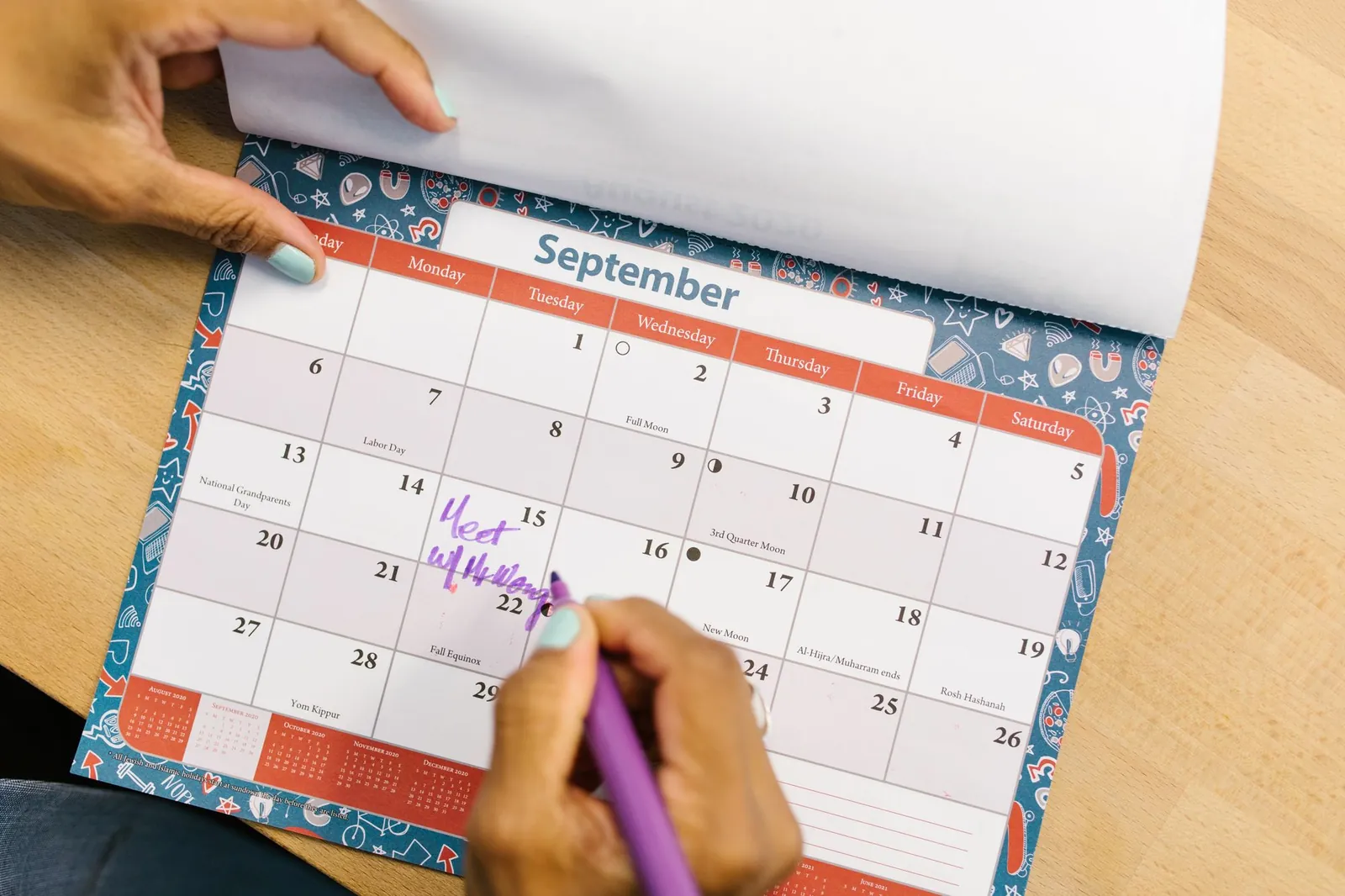 Hand schrijft in een maandkalender op een bureau
