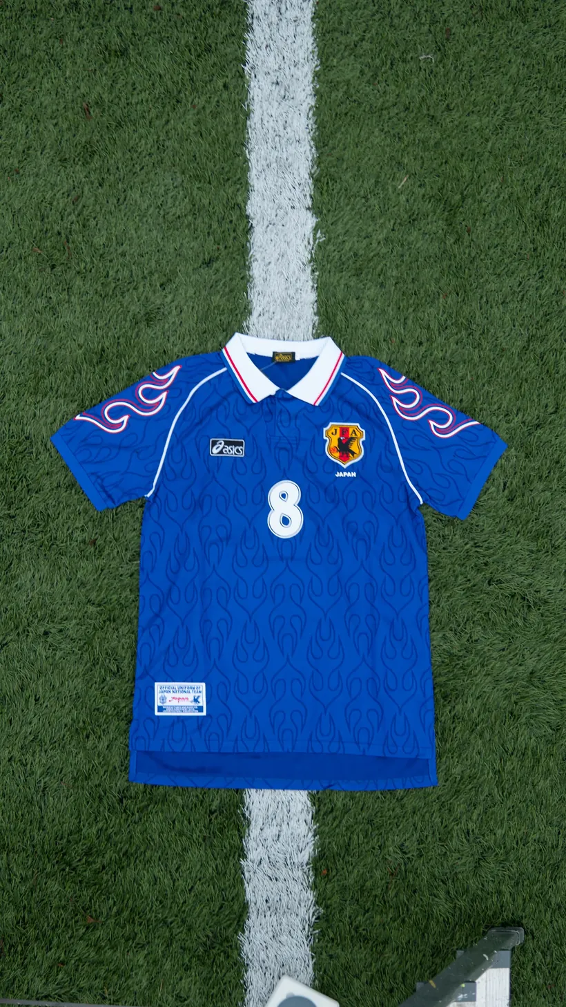 Blauw Japans voetbalshirt met rugnummer 8 plat op het gras naast een witte lijn