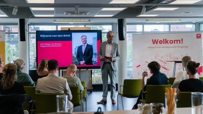 Zaal met groene stoelen en een welkomstbanner tijdens een evenement op Hogeschool Rotterdam