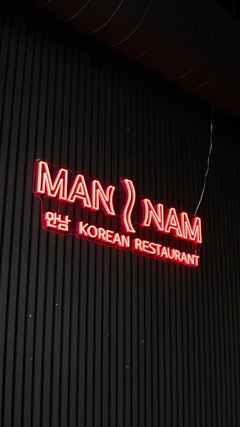 Rood neonbord van Man Nam Korean Restaurant tegen een zwarte lattenwand