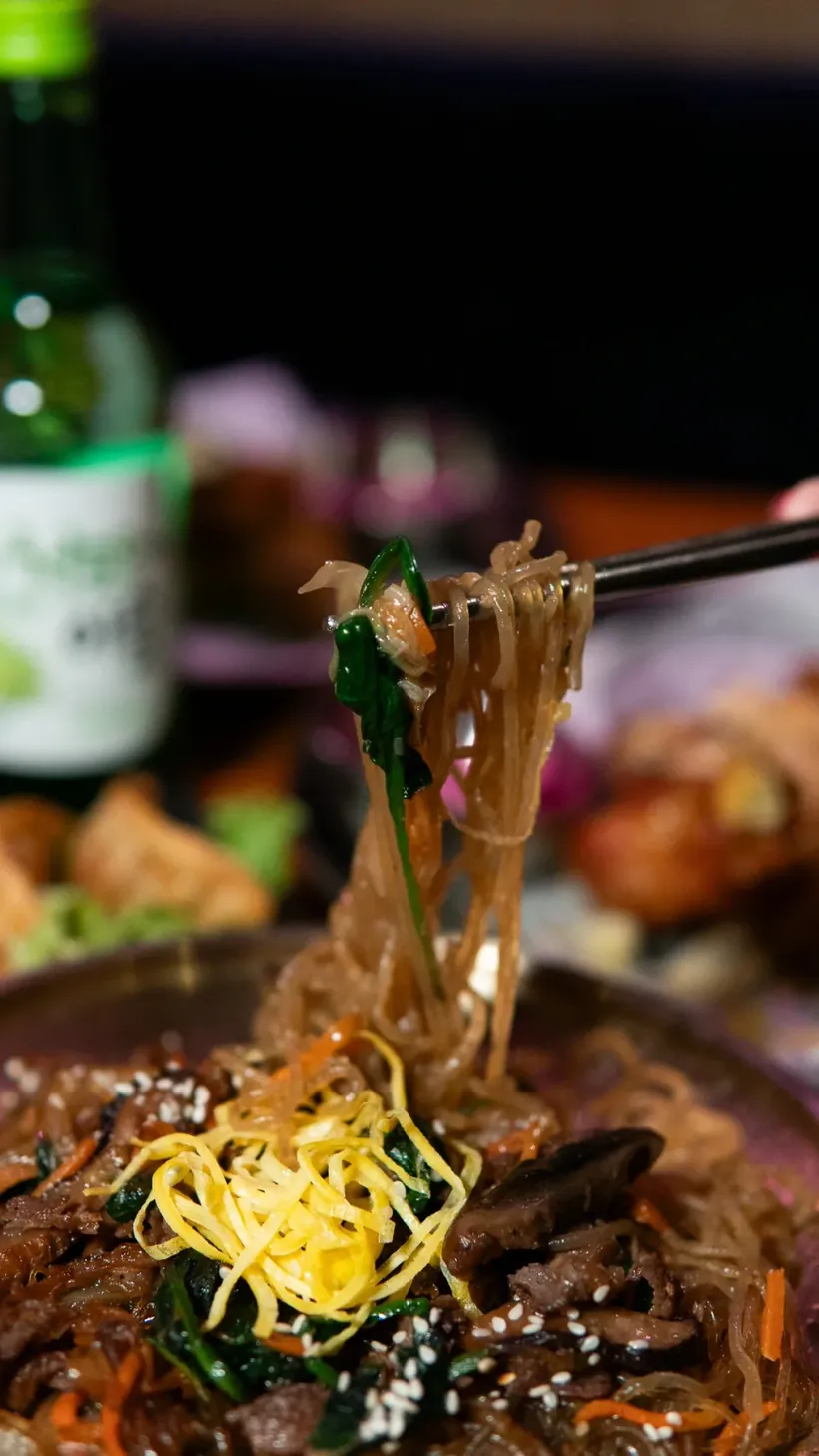 Glasnoedels die met stokjes uit een Koreaans gerecht worden opgetild