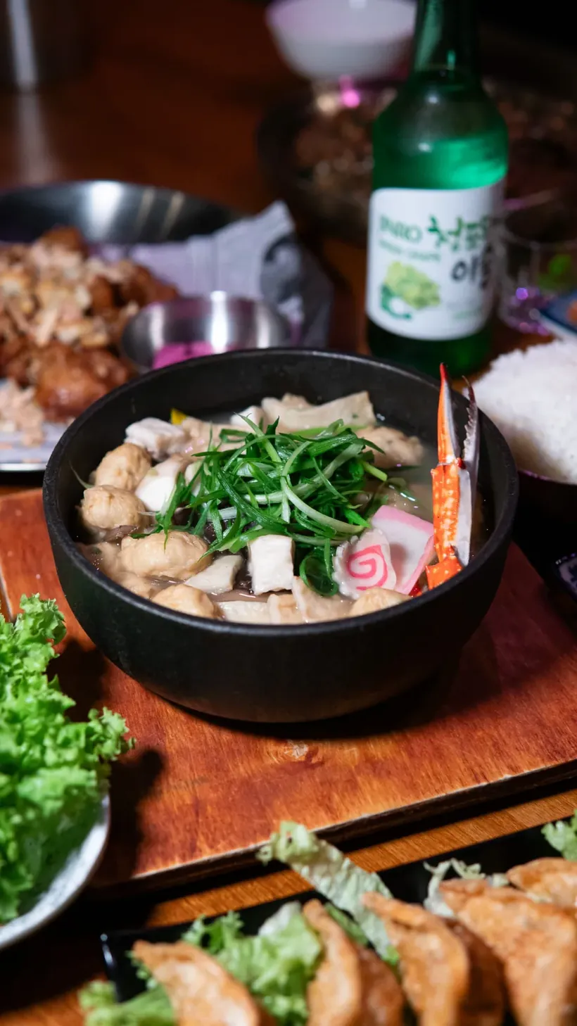 Koreaanse soep met lente-ui, dumplings en sla op een houten tafel met een fles soju