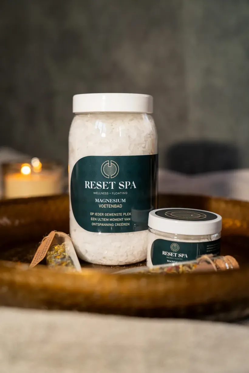 Pot badzout van Reset Spa naast een koperen schaal en een brandende kaars