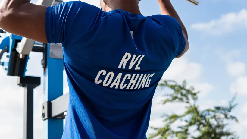 Sporter van achteren in een blauw shirt van RVL Coaching aan een fitnesstoestel in de buitenlucht