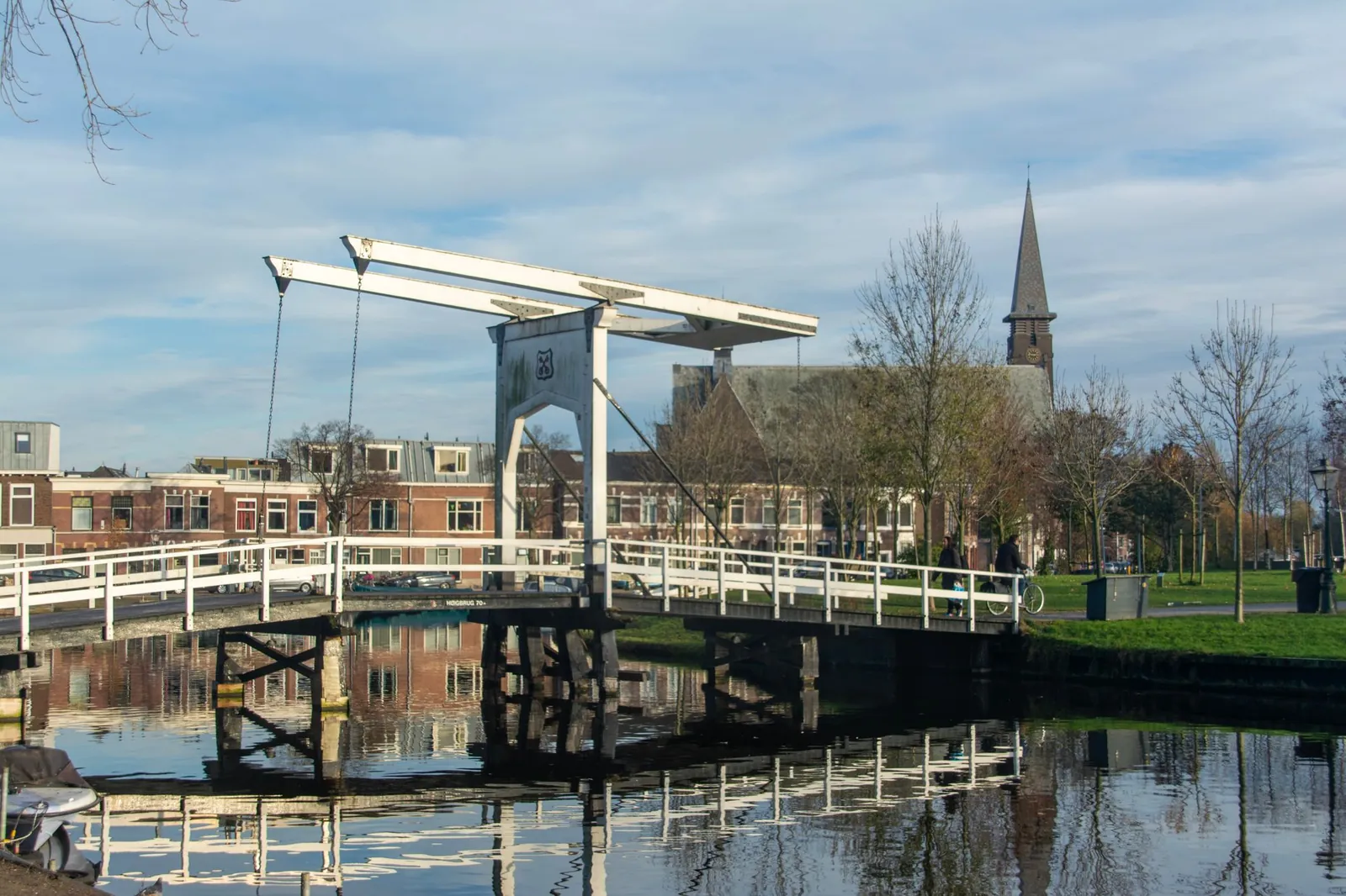Witte ophaalbrug over een gracht in Leiden met een kerktoren op de achtergrond