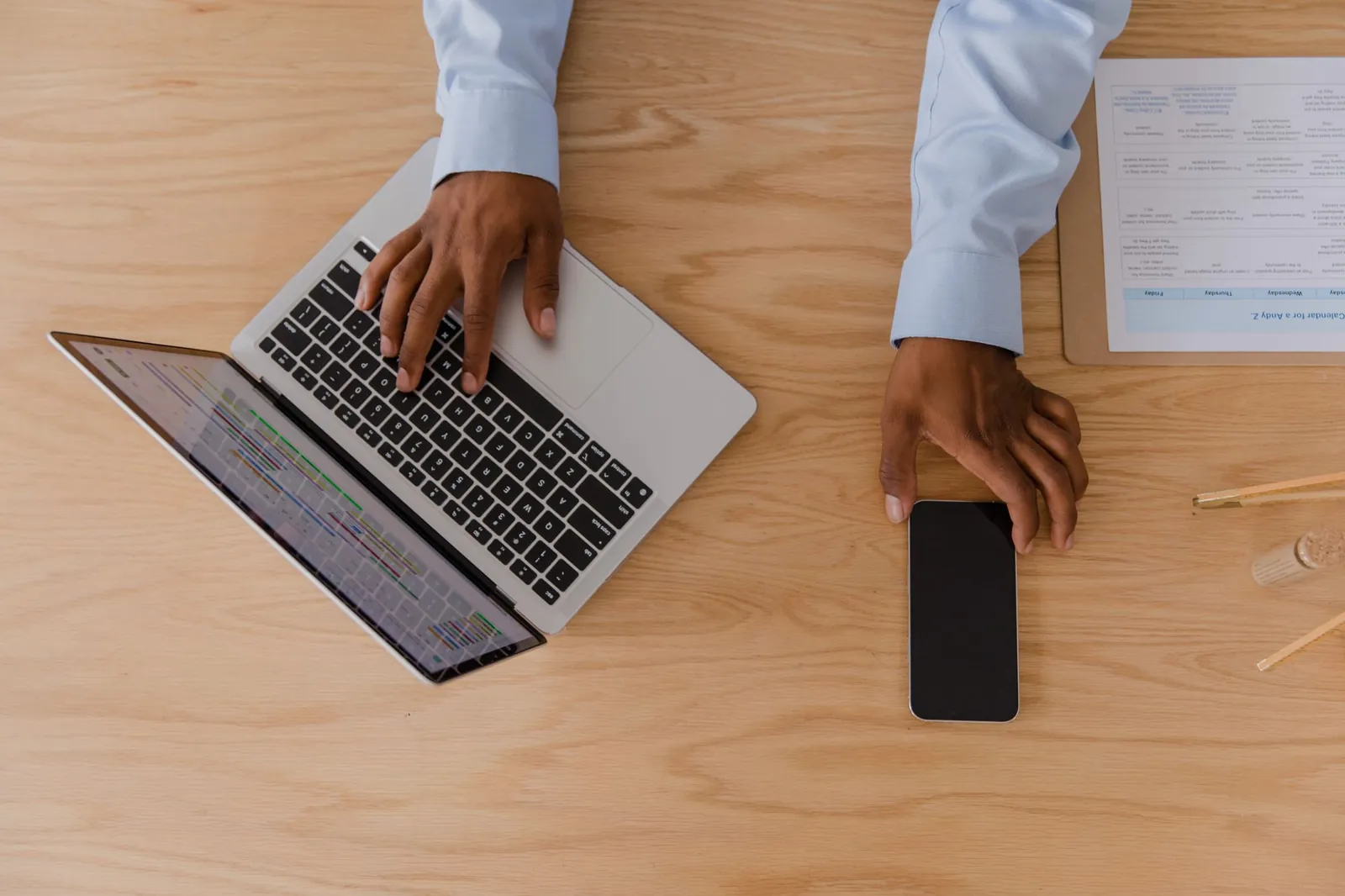 Handen met een laptop en een telefoon op een houten bureau