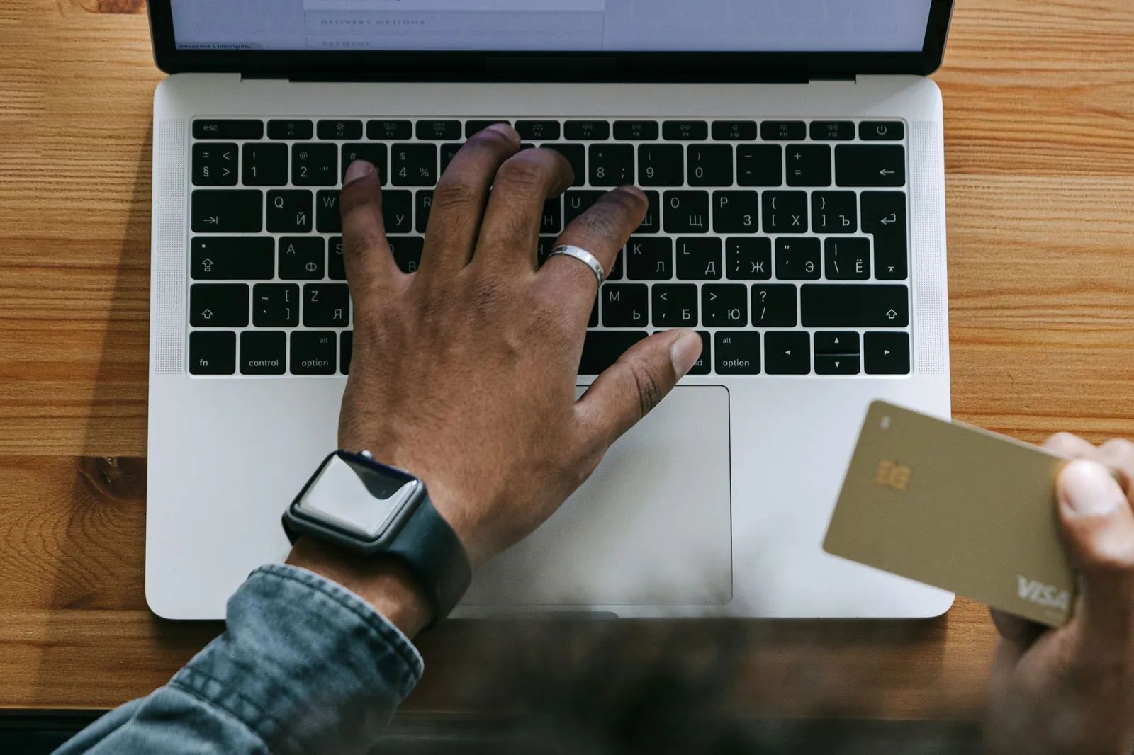 Hand met een bankpas boven een laptop tijdens online winkelen