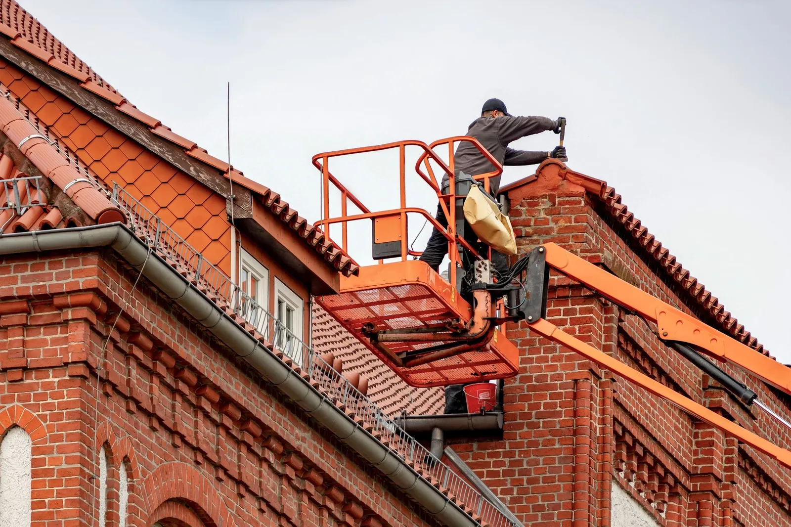 Dakdekker op een hoogwerker werkt aan het pannendak van een bakstenen gebouw