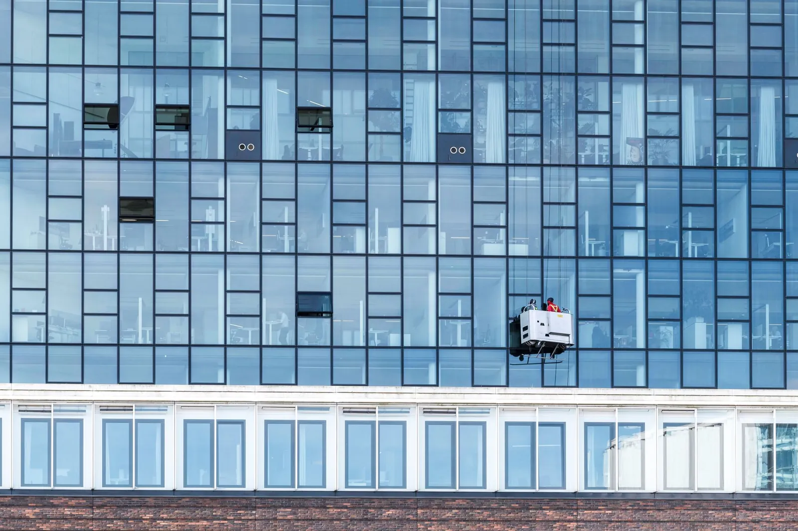 Glazen kantoorgebouw met glazenwassers op een hoogwerker