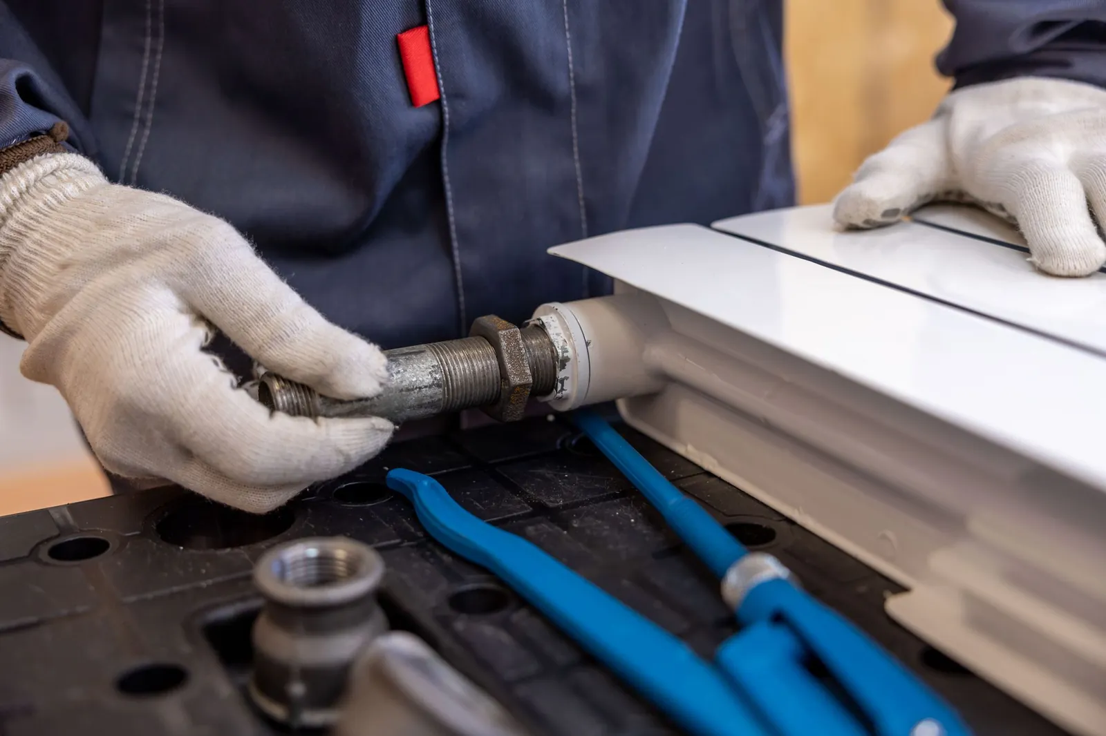 Handen in werkhandschoenen draaien een koppeling aan een radiatorleiding