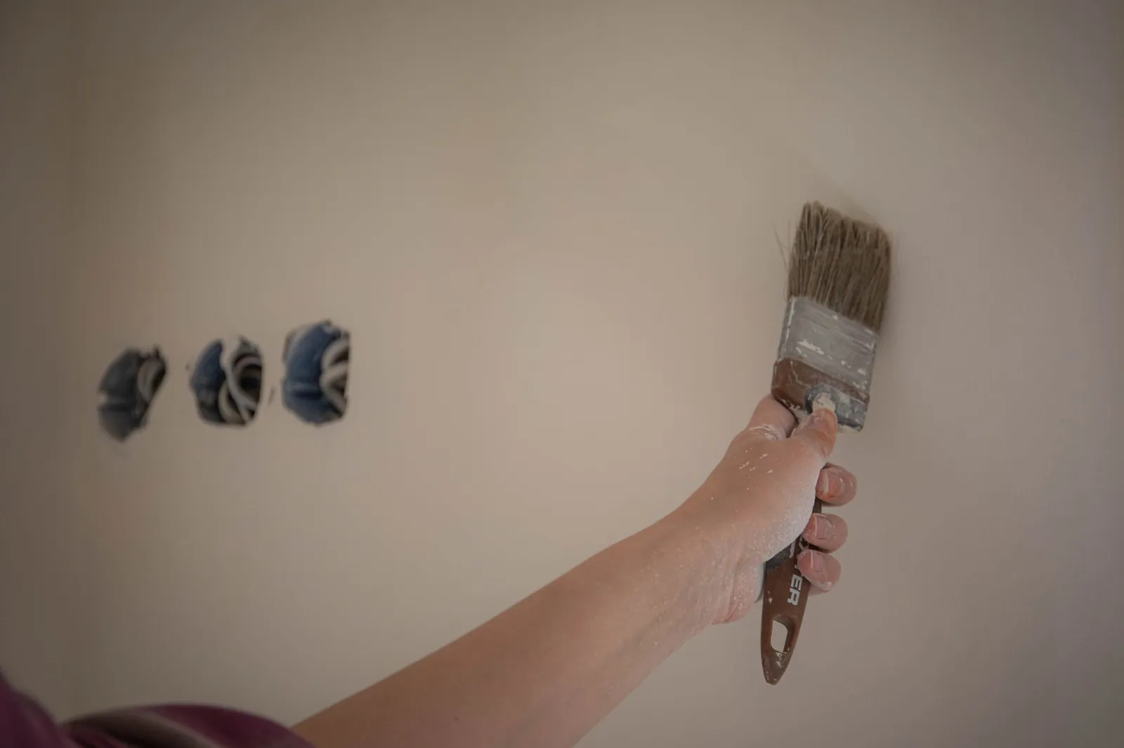 Hand met een kwast bij een lichte muur die geschilderd wordt
