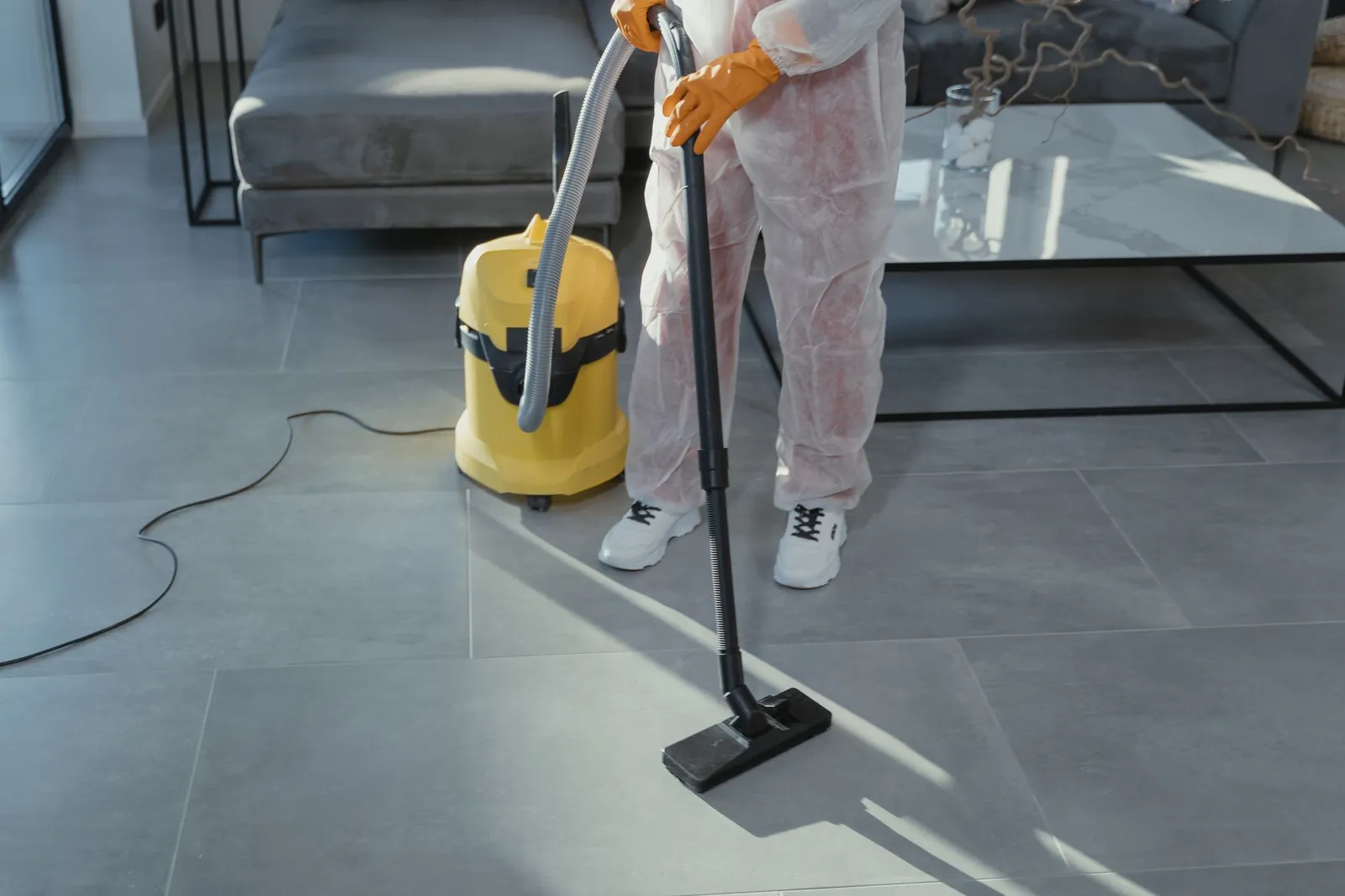 Schoonmaker met een stofzuiger in een lichte ruimte, van de schouders naar beneden