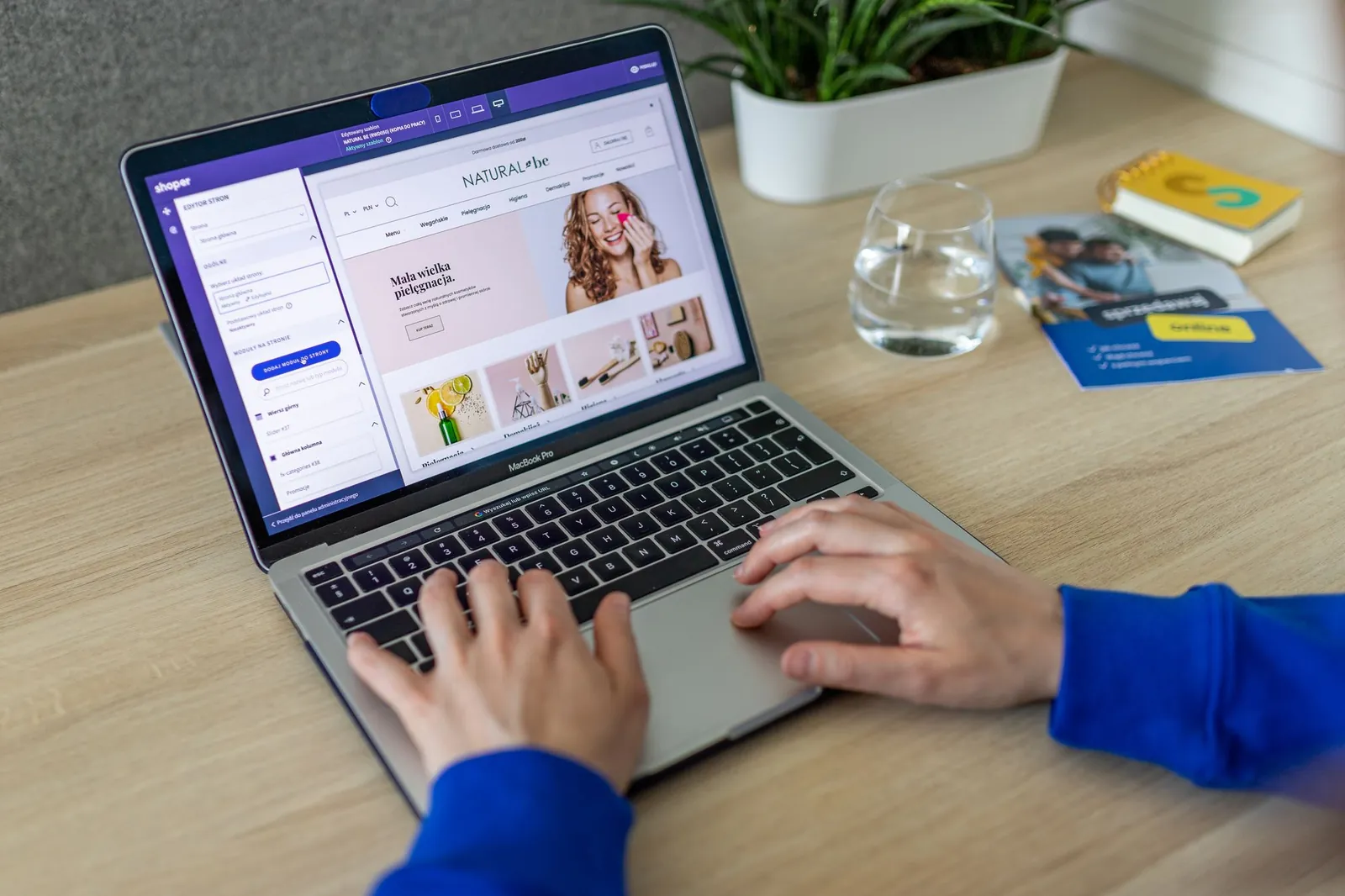 Handen op een laptop met een websitebouwer open, naast een kopje en planten