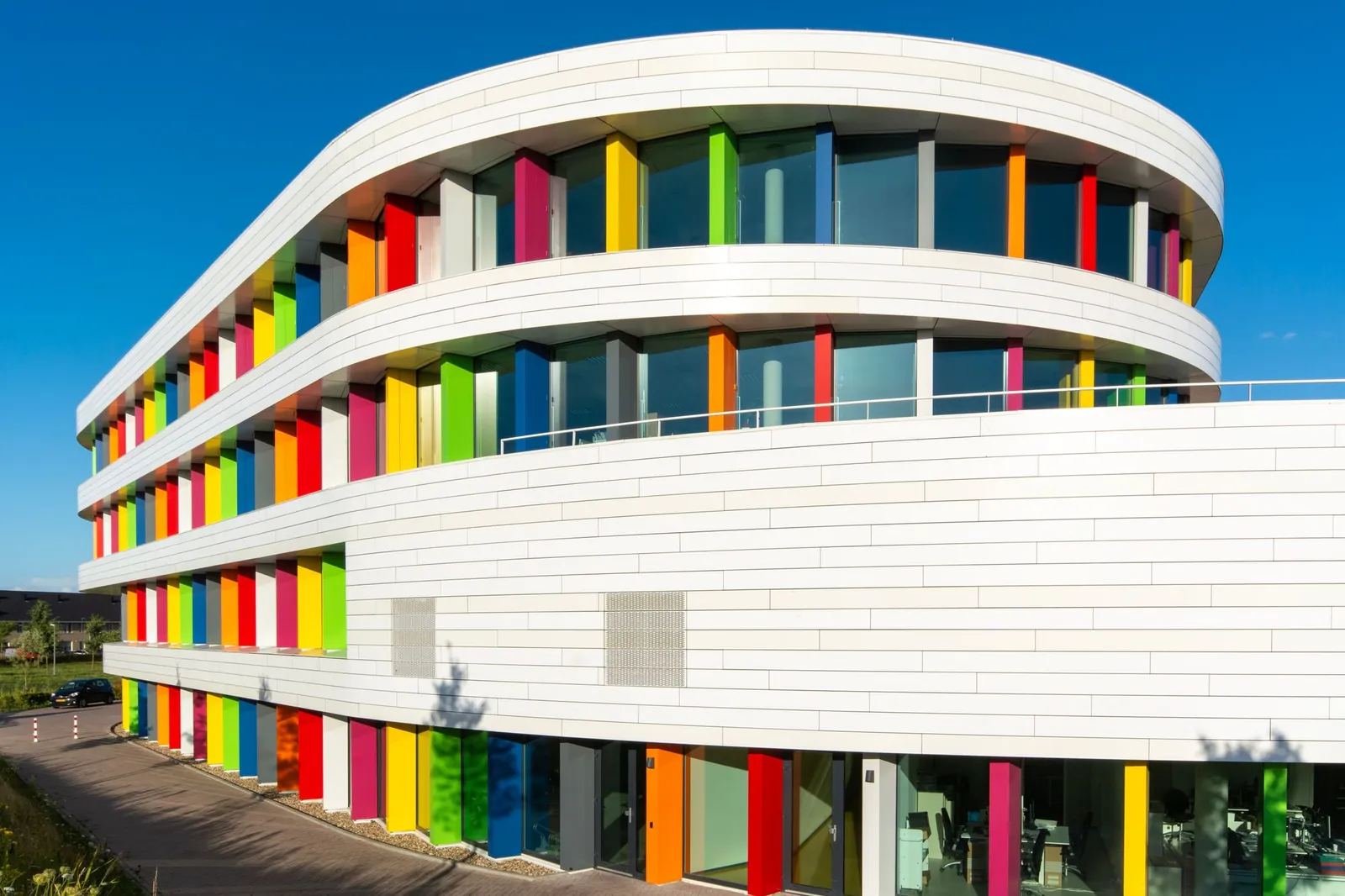 Wit kantoorgebouw met gekleurde gevelpanelen onder een blauwe lucht